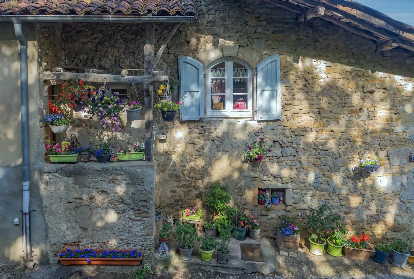 Façade en pierre aux volets bleus et fleurs (photo d'illustration)